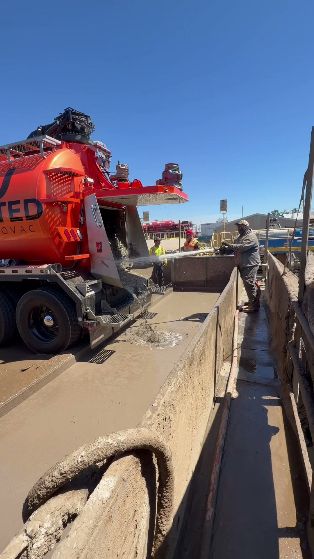 Crew member offloading slurry from an orange United Hydrovac vacuum truck into a concrete washout bay